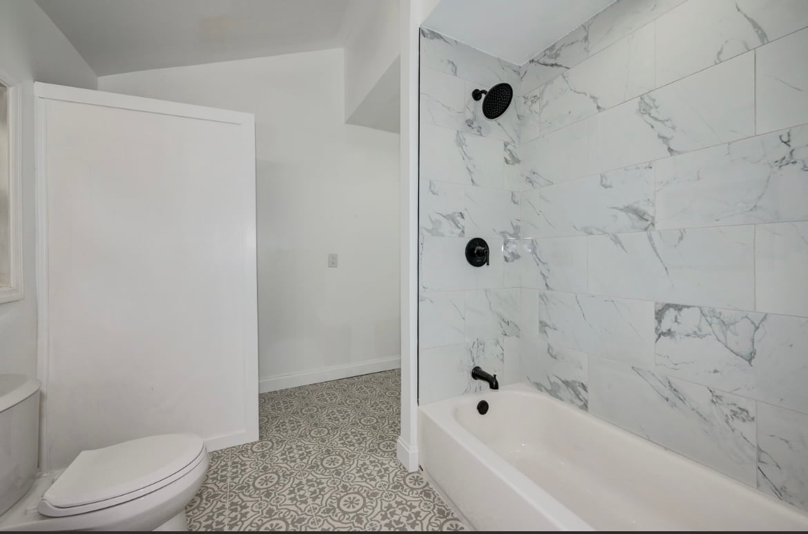 Modern bathroom with white toilet, marble-tiled shower enclosure, and terrazzo tile flooring
