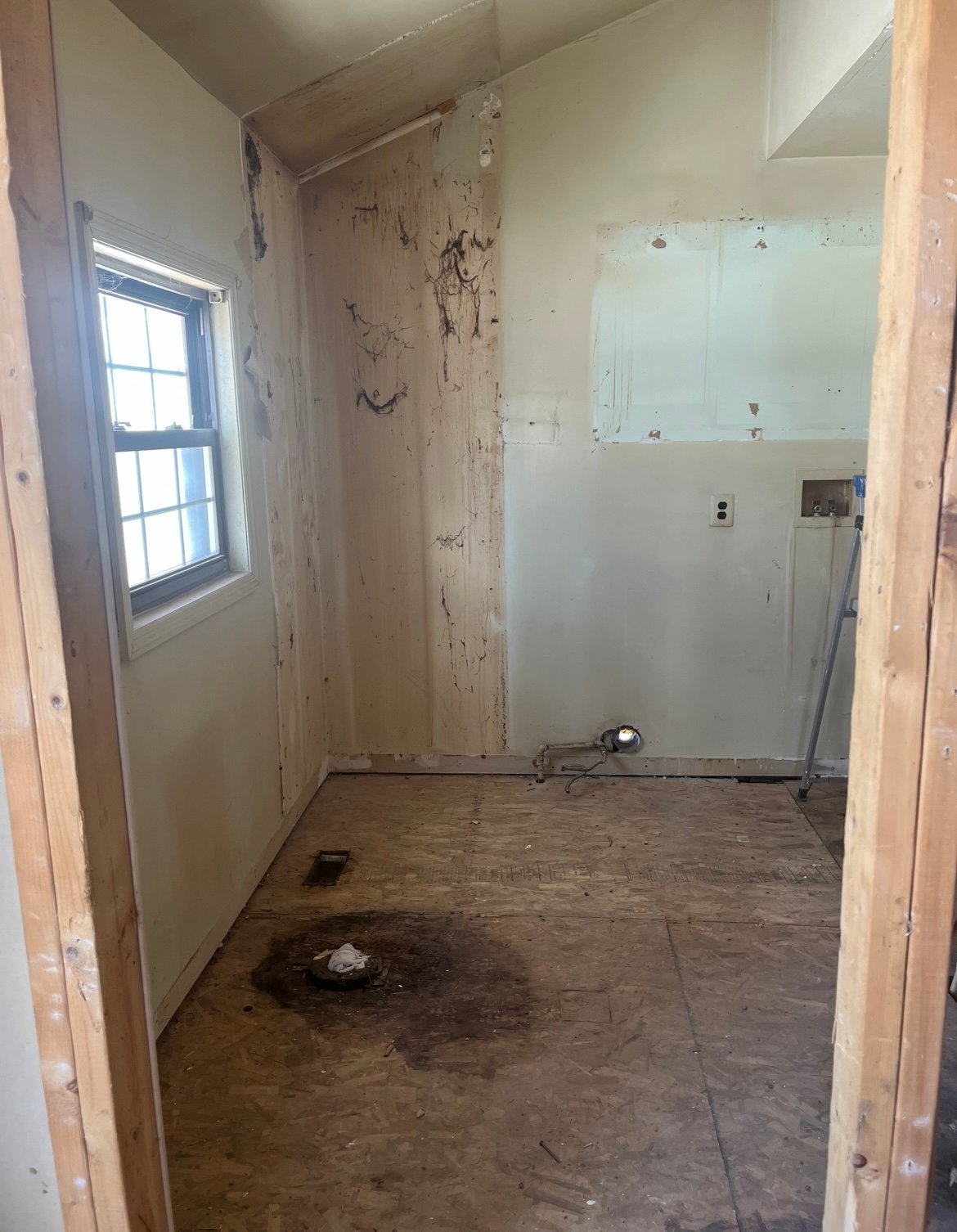 Unfinished bathroom under renovation with bare drywall, exposed framing, concrete floor, and a window on the left wall