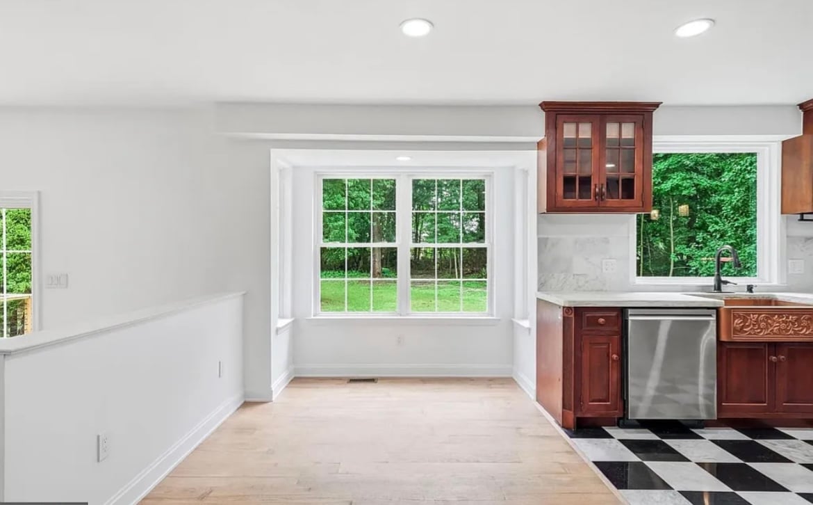 Modern kitchen with red wood cabinetry, black and white checkered floor, and french doors with windows overlooking green landscape