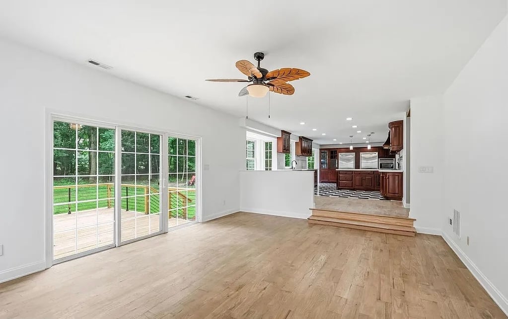 Bright open living room with hardwood floors, multi-pane glass doors, ceiling fan, and kitchen visible in background