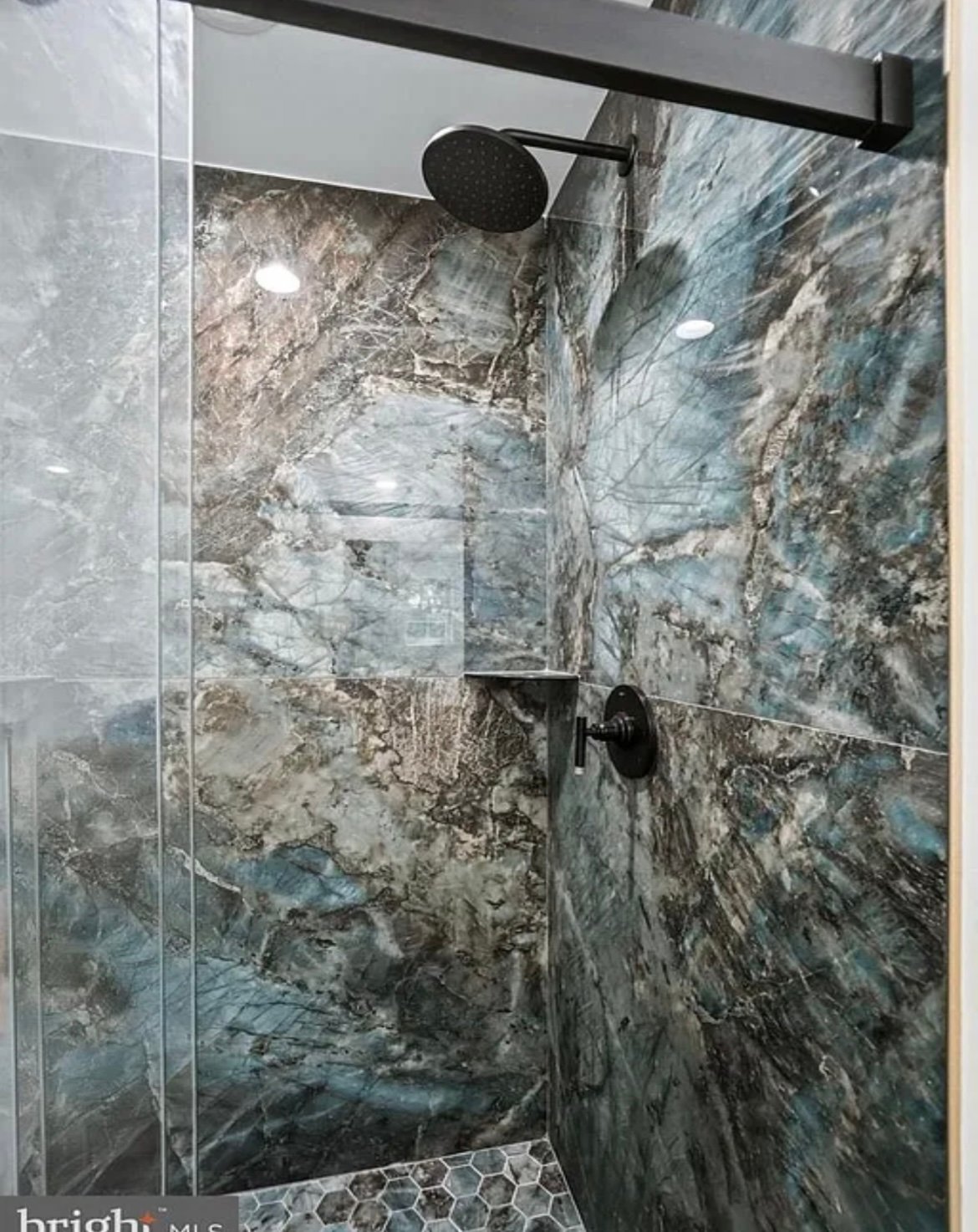Modern bathroom shower with gray marble-effect tile walls, black fixtures, and glass enclosure doors