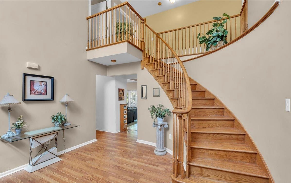 Modern home interior with curved wooden staircase, hardwood floors, console table with plants, and mezzanine balcony overlooking entry foyer