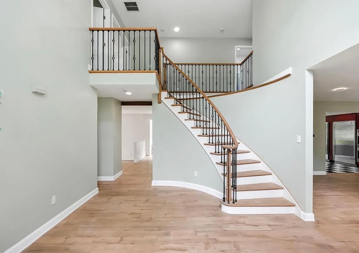 Modern interior with wooden staircase, metal railings, and hardwood flooring in an open floor plan entryway.