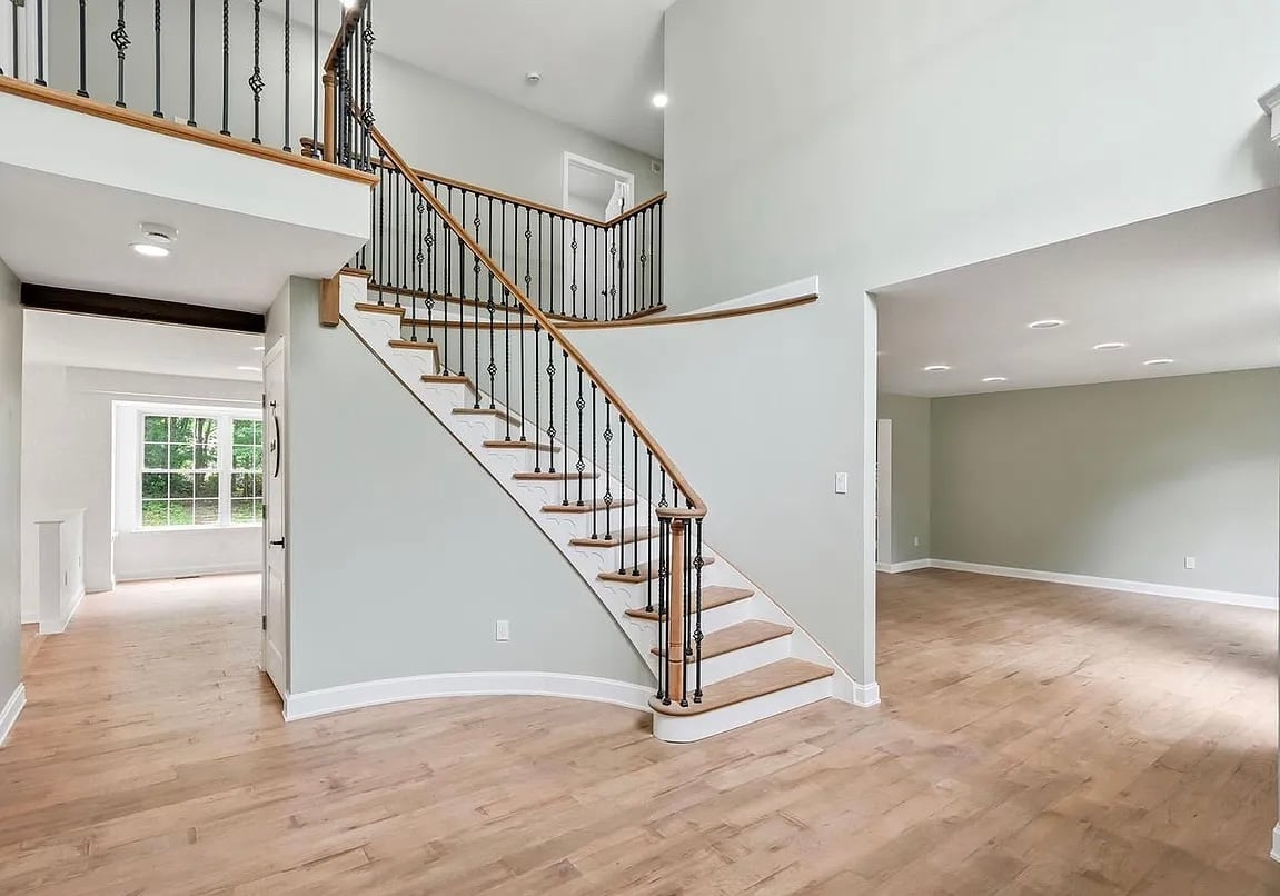 Modern two-story foyer with wooden staircase, black railings, wood flooring, and open living spaces