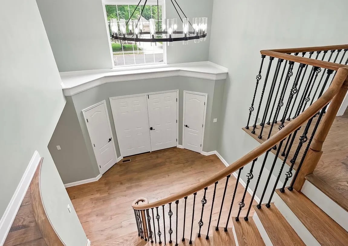 View of a curved staircase with wooden banister leading down to a foyer with white built-in cabinets and a window above