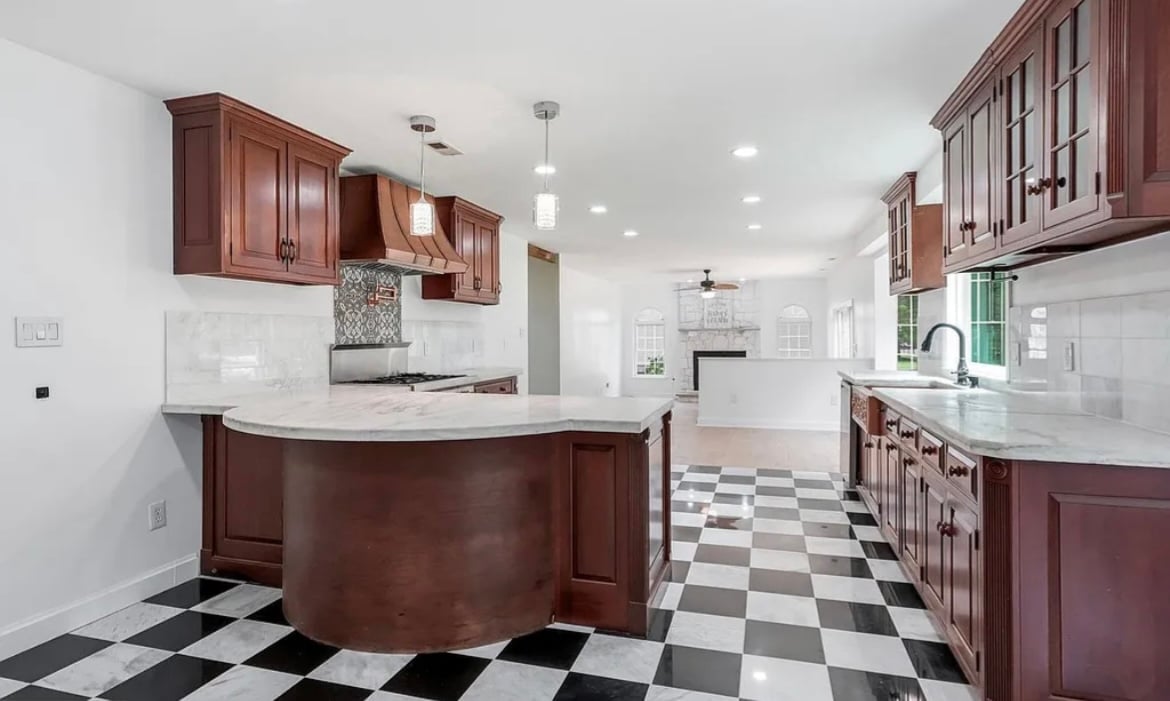 Modern kitchen with dark cherry wood cabinetry, large center island, black and white checkered floor, and stainless steel appliances