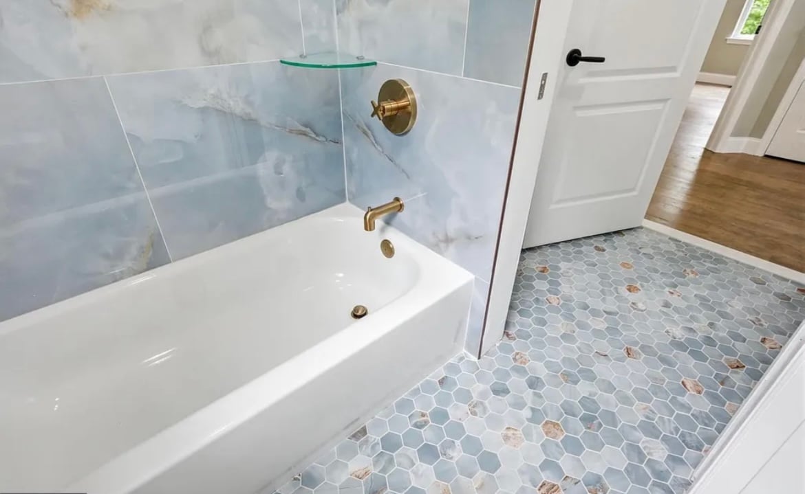 Modern bathroom with white bathtub, glass shower enclosure, hexagonal tile flooring, and brass fixtures