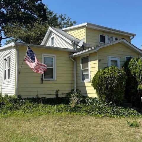 Pale yellow two-story house with American flag, surrounded by green lawn and hedges on a clear day