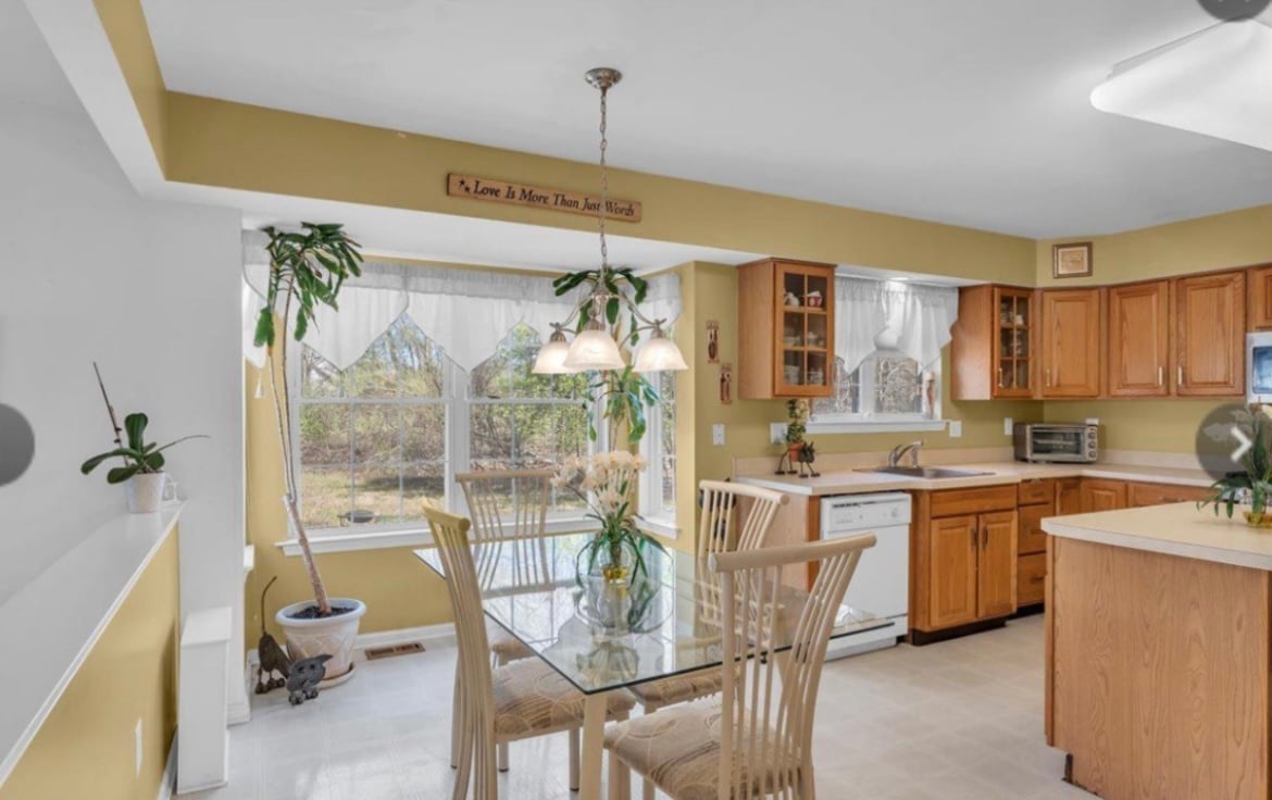 Bright kitchen with wooden cabinets, white counters, and large windows overlooking a deck with outdoor furniture