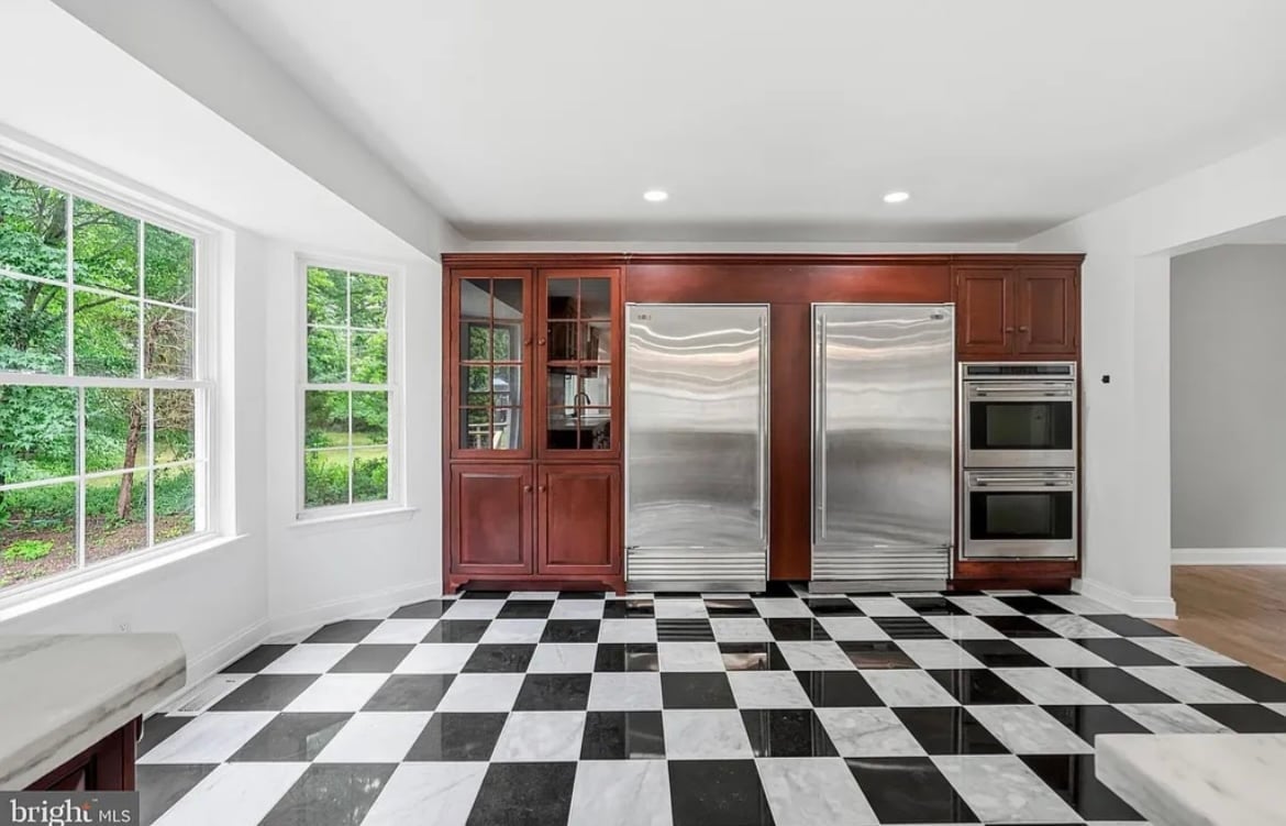 Luxury kitchen with black and white diamond-patterned floor, cherry wood cabinetry, stainless steel appliances, and large windows overlooking greenery